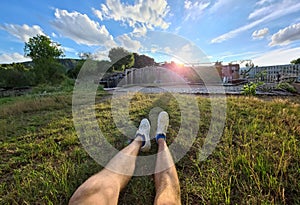 Male feet in white sneakers lying on green grass against background of waterfall closeup