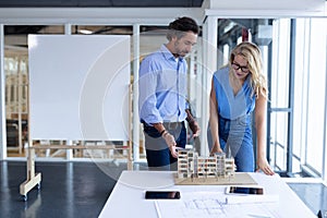 Male and female architect discussing over architectural model at table in a modern office