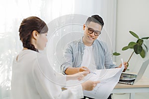 Male and female architect discussing a set of blueprints spread out on a table at office