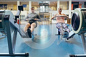 Male and female athlete exercising with rowing machine in fitness studio