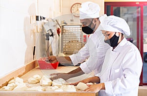 Male and female baker in protective mask working together in bakery