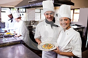 Male and female chefs holding plate of prepared pasta in kitchen