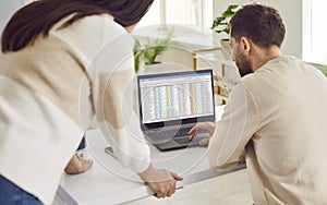 Male and female colleagues checking spreadsheet on laptop screen