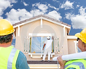 Male and Female Contractors Overlooking Painter Painting House photo