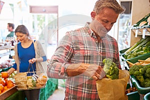 Male And Female Customers With Shopping Basket Buying Fresh Produce In Organic Farm Shop