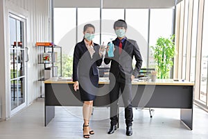 Male and female employee wearing medical face mask while holding alcohol hand gel and spray for hygiene workplace during virus and