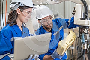 Male and female engineer training using remote controller control robot arm welding machine in industrial factory