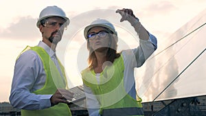 A male and a female engineers discussing solar energy standing near solar panels. Solar energy concept.