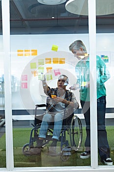 Male and female executives discussing over sticky notes in office