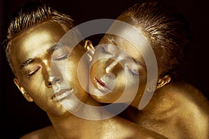 Male and female face around. The woman`s head lies on the shoulder of a man. All painted in gold paint, the feeling of a
