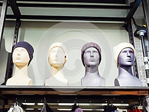 Male and female gray and white mannequin heads in knitted hats stand on a shelf