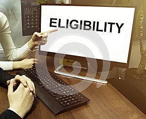 Male and female hand, computer with text Eligibility with office background photo