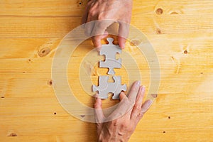 Male and female hand joining two matching puzzle pieces over yellow wooden background