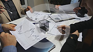 Male and female hands of coworkers examining graphs at the end of working day. Business team sitting at table and