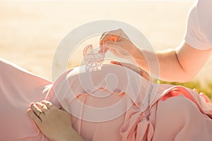 Male and female hands hold a pregnant belly closeup and copy space. Pregnant in a pink dress and male hands with a miniature strol