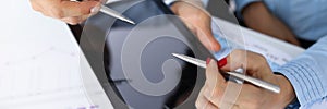 Male and female hands are holding ballpoint pens over tablet on table in office closeup