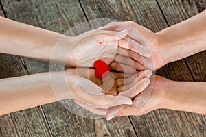 Male and female hands holding red heart on wooden background