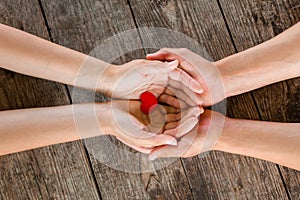 Male and female hands holding red heart on wooden background