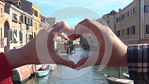 Male and female hands showing heart shape on the background of beautiful view of Venice. Symbol of love. Couple