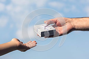 Male and female hands with a small white gift boxe on the blue sky background.