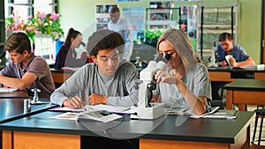 Male And Female High School Students Using Microscope In Biology Class
