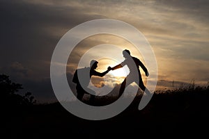 Male hikers climbing up mountain cliff and one of them giving helping hand.