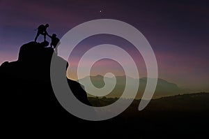 Male and female hikers climbing up mountain cliff and one of the