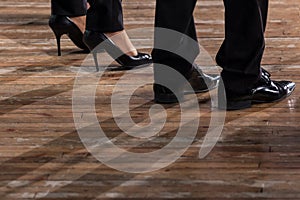 Male and female legs in black shoes and trousers on an old wooden parquet floor. Close-up.