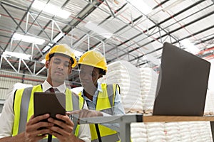 Male and female manager discussing over digital tablet at desk in warehouse