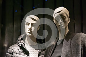 Male and female mannequins in a store window wearing dark clothes. Man and woman.