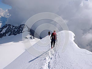 Male and female mountain climber descending from a high alpine summit along a narrow snow and ice ridge