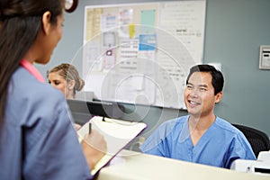 Male And Female Nurse In Discussion At Nurses Station