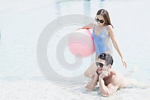 Male and female playing in the pool with a beach ball. Young couple embracing in the pool