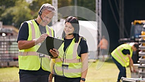 Male And Female Production Team With Headsets Setting Up Outdoor Stage For Music Festival Or Concert