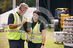 Male And Female Production Team With Headsets Setting Up Outdoor Stage For Music Festival Or Concert