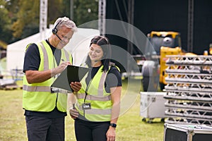 Male And Female Production Team With Headsets Setting Up Outdoor Stage For Music Festival Or Concert