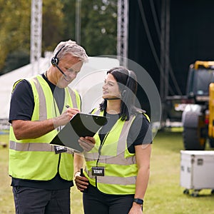 Male And Female Production Team With Headsets Setting Up Outdoor Stage For Music Festival Or Concert