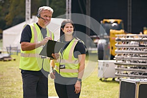 Male And Female Production Team With Headsets Setting Up Outdoor Stage For Music Festival Or Concert