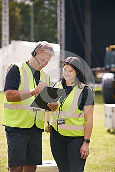 Male And Female Production Team With Headsets Setting Up Outdoor Stage For Music Festival Or Concert