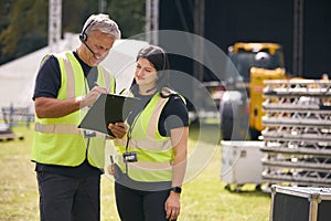 Male And Female Production Team With Headsets Setting Up Outdoor Stage For Music Festival Or Concert