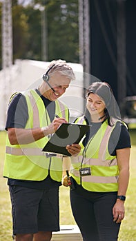 Male And Female Production Team With Headsets Setting Up Outdoor Stage For Music Festival Or Concert