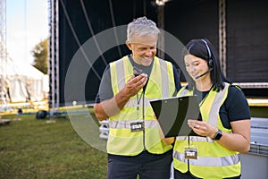 Male And Female Production Team With Headsets Setting Up Outdoor Stage For Music Festival Or Concert