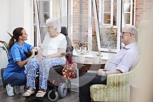 Male And Female Residents Sitting In Chair And Talking With Nurse In Retirement Home