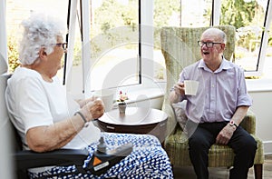 Male And Female Residents Sitting In Chairs and Talking In Retirement Home