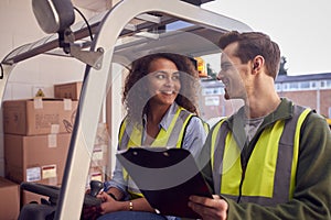 Male And Female Staff Operating Fork Lift Truck In Modern Warehouse