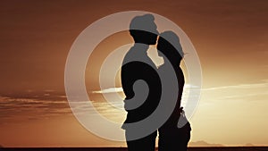 Male and female stand in an embrace in the morning near the sea. Silhouette of a loving family at sunrise or sunset