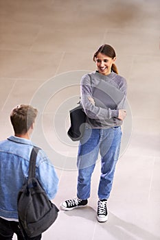 Male And Female Students In Busy University Or College Building Talking As They Meet In Corridor