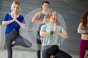 Male and female students doing yoga exercise in college sport hall standing in Tree Pose