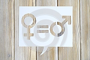 Male and female symbols and an equal sign in white dialogue box cut out of paper on a wooden background. the concept of gender equ