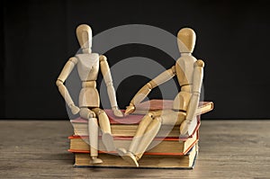 Male and female wooden mannequins sitting on books